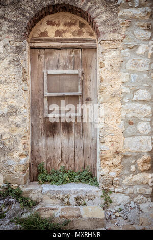 Alte braune Holztür und schmutzige Mauer aus Stein. Pflanzen, die in der vorderen Tür und zwei steinerne Stufen. Eingang zum Haus Stockfoto