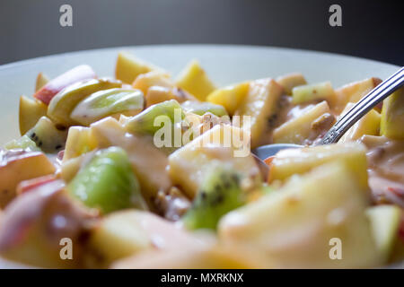 Mit gehackten Äpfel und Kiwis mit Müsli und Joghurt gemischte Platte. Eine Stahl spoon Rest in der Frucht. Stockfoto