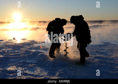 Hochrangige Flieger und Unteroffiziere der 354th Civil Engineer Squadron in Eielson AFB, Alaska, bohren mit einer Schnecke durch den gefrorenen Tanana River. Freiliegendes Wasser wird verwendet, um Eis zu bilden und eine stabile Eisbrücke für den Transport von Personal, Ausrüstung und Vorräten zum Blair Lakes Range Maintenance Complex zu schaffen. Die Operation unterstützt die Arctic Range Maintenance, Mission Continuity, operative Sicherheit und logistische Effizienz für den 354th Fighter Wing. Stockfoto