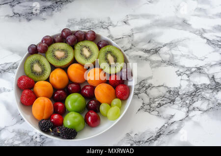 Frische bunte Früchte in weiße Platte. Es gibt Aprikosen, Erdbeeren, Trauben, Kirschen, Pflaumen, Kiwi, Maulbeeren in der Platte. Stockfoto