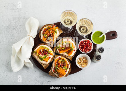 Snack Brote mit Hummus und gebackenen Kürbis auf einer Platine mit Rucola Pesto. Samen von Granatapfel und Pinienkernen. Gesund Essen und Wein Stockfoto