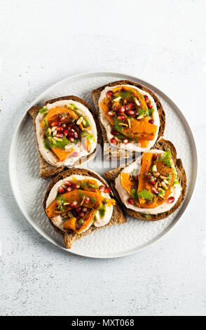 Snack Brote mit Hummus und gebackenen Kürbis auf einer Platine mit Rucola Pesto. Samen von Granatapfel und Pinienkernen. Gesundes Essen Stockfoto