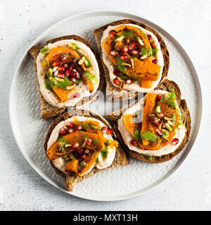 Snack Brote mit Hummus und gebackenen Kürbis auf einer Platine mit Rucola Pesto. Samen von Granatapfel und Pinienkernen. Gesundes Essen Stockfoto