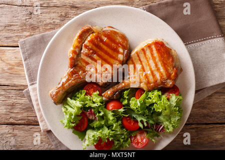 Gegrilltes Kotelett Schwein Honey Glaze, serviert mit Salat von frischem Gemüse close-up auf einem Teller auf dem Tisch. horizontal oben Ansicht von oben Stockfoto