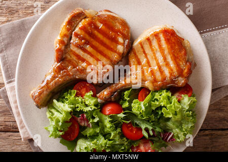 Köstliche Honig Schweinefleisch vom Grill mit Salat von frischem Gemüse in der Nähe serviert auf einem Teller auf den Tisch hacken. Horizontal oben Ansicht von oben Stockfoto