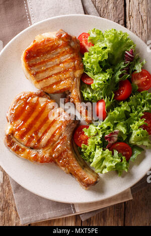 Köstliche Honig Schweinefleisch vom Grill mit Salat von frischem Gemüse in der Nähe serviert auf einem Teller auf den Tisch hacken. Vertikal oben Ansicht von oben Stockfoto