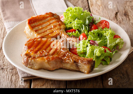 Gegrilltes Schweinesteak mit einem Knochen in einem süßen Honig glasieren und einem Salat von frischem Gemüse close-up auf einem Teller auf dem Tisch. Horizontale Stockfoto