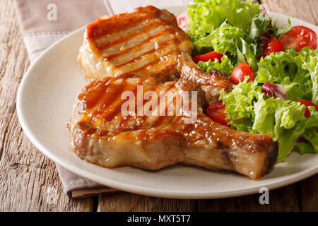 Grill essen: ein gegrilltes Schweinefleisch in süßen Honig chop Glasur und einem Salat von frischem Gemüse close-up auf einem Teller auf dem Tisch. Horizontale Stockfoto