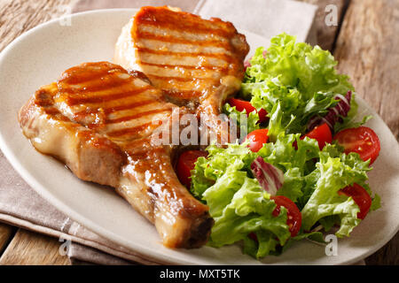 Köstliche Honig Schweinefleisch vom Grill mit Salat von frischem Gemüse in der Nähe serviert auf einem Teller auf den Tisch hacken. Horizontale Stockfoto