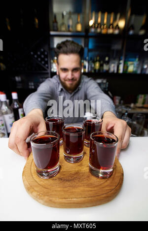 Alkoholische rot Schüsse auf ein Brett in die Hände eines bärtigen Barkeeper. Stockfoto