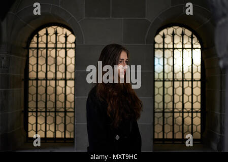 Junge westliche Frau in Schwarz gekleidet stand vor einer großen Kirche Fenster tief in Gedanken Stockfoto