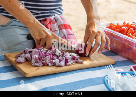 Frau Hände schneiden rote Zwiebeln auf dem hölzernen Schneidebrett. Koch hacken eine rote Zwiebel mit einem Messer für Gemüse Salat. Street Food Festival. Stockfoto