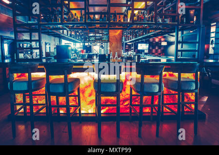 Die Vorderansicht der stilvollen Bar Zähler mit der Bar aus Holz Stühle auf die voll ausgestattete Bar Hintergrund. Modern im Dekor des modernen Restaurant. Golden Orange, dunkelblau Tönungen. Stockfoto