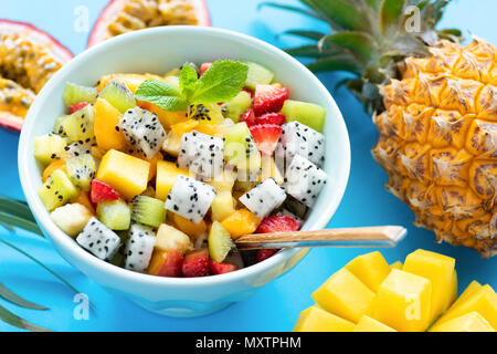 Obst Salat in der Schüssel auf blauem Hintergrund. Exotischen tropischen Obstsalat. Dragon Obst, Passionsfrucht, Mango, Kokos, Erdbeeren und Ananas Salat in Einem Stockfoto