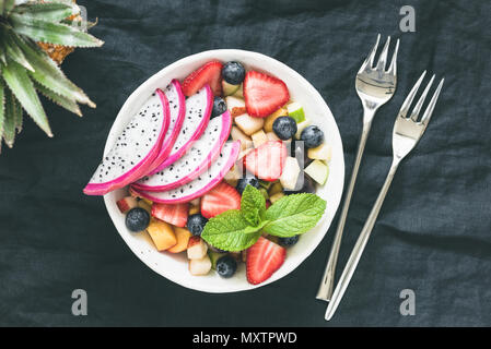 Tropischer Obstsalat mit Dragon Obst in einer Schüssel auf dunklem Hintergrund, getönten Bild. Tabelle Blick von oben auf die gesunde vegane Obstsalat Stockfoto