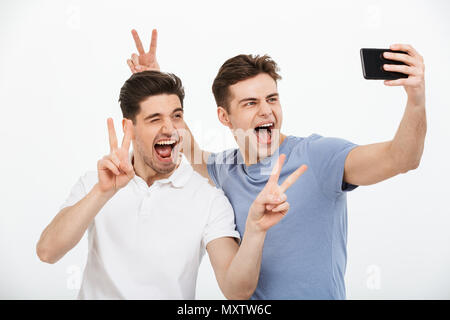 Porträt von zwei glückliche junge Männer mit Frieden Geste während der Einnahme eines selfie auf weißem Hintergrund Stockfoto