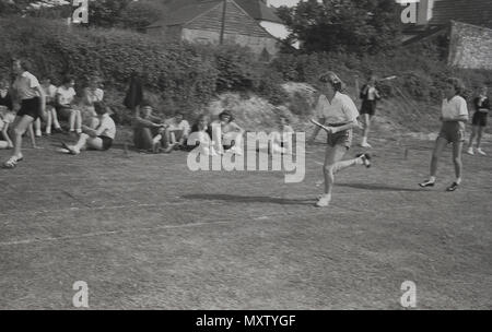 1960, historische Bild von sekundärschoolgirls, die an einem Staffellauf in einem inter-Schule county Sports Day, Dorset, England, UK. Eines der Mädchen wird gezeigt, Durchführung der Staffelstab in der linken Hand, während er so schnell Sie können auf dem Rasen verfolgen. Stockfoto