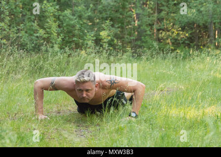 Mitte Barechested nach 40 s kaukasischen Mann tun Push-ups auf Gras draußen in Wald Wiese Stockfoto