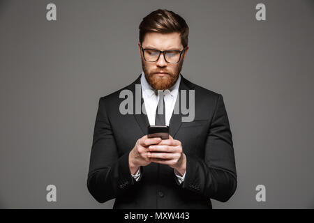 Porträt einer selbstbewussten jungen Geschäftsmann mit Mobiltelefon über grauen Hintergrund isoliert Anzug Stockfoto