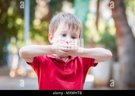 Ernsthafte wenig Kaukasischen Junge seinen Mund mit den Händen zu schließen. Anschauliches Bild für kindheitstrauma Konzept, Kind traumatische Erfahrung. Psychologische Stockfoto