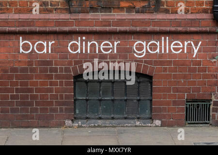 Eine rote Mauer mit einer vergitterten Fenster in einen Keller Restaurant oder Bar, Restaurant, Galerie auf der Straße im Zentrum von London. Keller oder Untergeschoss Diner. Stockfoto