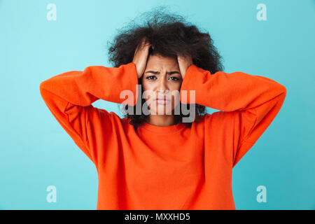 Bild Nahaufnahme der frustrierten Frau in Rot shirt Suchen auf Kamera und packte den Kopf mit zotteligen Haaren über blau Hintergrund isoliert Stockfoto