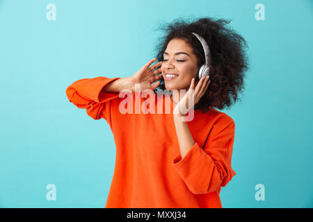 Junge amerikanische Frau 20s mit Zotteligen Frisur Musik über kabellose Kopfhörer hören Lieblingstitel über blau Hintergrund isoliert Stockfoto