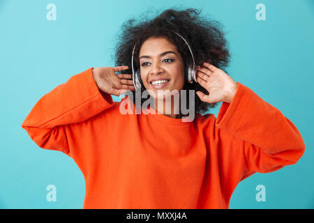 Gerne amerikanische Frau 20s mit Zotteligen Frisur Musik über kabellose Kopfhörer hören Lieblingstitel über blau Hintergrund isoliert Stockfoto