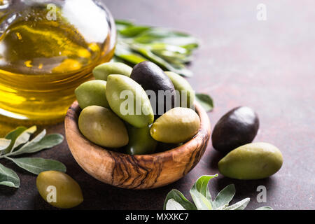 Schwarze und Grüne Oliven in eine Schüssel geben und das Olivenöl Flasche auf dunklem Stein Tabelle. Close Up. Stockfoto