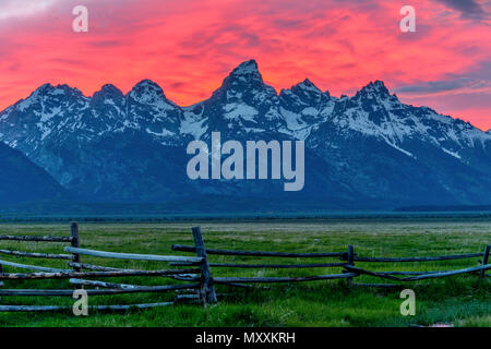 Grand Teton - Dämmerung Blick auf Teton Bergkette gegen hellen roten Sonnenuntergang Wolken, aus einem alten Ranch in Mormonischen Reihe, Grand Teton National Park gesehen. Stockfoto