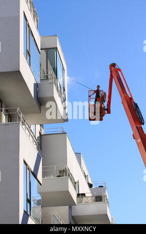 Kopenhagen, Dänemark - 8. Mai 2018: Mann Reinigung Fassade eines modernen minimalistischen Apartment Gebäude auf einem Teleskoparm heben mit Druck jet Wash b Stockfoto