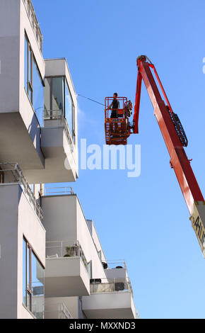 Kopenhagen, Dänemark - 8. Mai 2018: Mann Reinigung Fassade eines modernen minimalistischen Apartment Gebäude auf einem Teleskoparm heben mit Druck jet Wash b Stockfoto