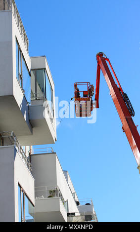 Mann Reinigung Fassade eines modernen minimalistischen Apartment Gebäude auf einem Teleskopausleger mit Druck jet Wash mit blauer Himmel heben Stockfoto