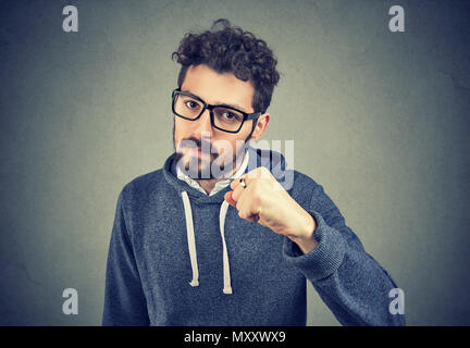 Junger Mann in Gläser holding Faust Bärtigen, mit Ernst Bedrohung auf grauem Hintergrund. Stockfoto