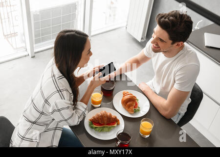Bild von oben fröhliche, Mann und Frau, die Abendessen zu Hause in der Küche mit Smartphone in der Hand Stockfoto