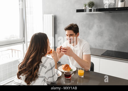 Portrait von freuen Paar schauen einander an und lächelte, während er in der Küche mit dem Essen auf dem Tisch Stockfoto