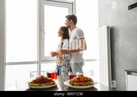 Ehepaar stand und durch große Fenster beim Frühstück in moderne Wohnung in Morgen Stockfoto