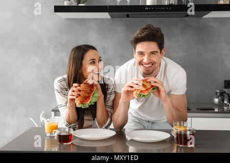 Junge und schöne Paar lächelnd und Sandwiches essen auf das Frühstück in der Küche Stockfoto