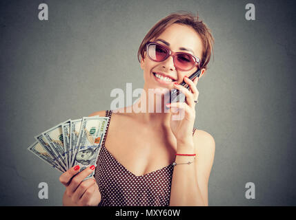 Stilvolle Frau in Sonnenbrille holding Haufen von Dollar und sprechen auf dem Smartphone Suche erfolgreich. Stockfoto