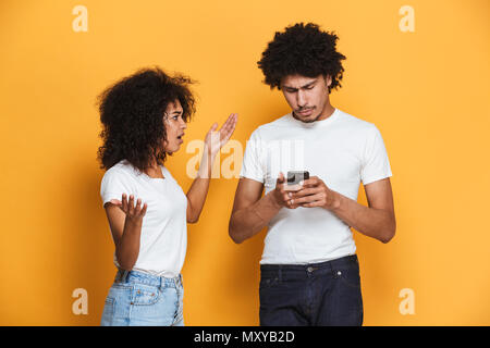 Porträt eines frustrierten jungen afro-amerikanische Paar in ein Argument, weil von Handy über Gelb Hintergrund isoliert Stockfoto