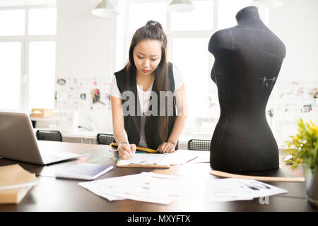 Taille bis Portrait von fokussierten asiatische Frau arbeiten in Modedesign und Skizzen an Schneider Tabelle steht durch Nähen dummy in der modernen Atelier st Stockfoto