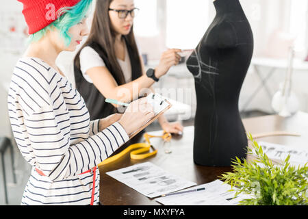 Taille, Porträt von zwei modernen kreativen jungen Frauen arbeiten in Fashion Design und Zusammenarbeit an Projekt stand von Schneidern Tabelle in Moder Stockfoto