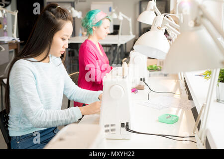 Porträt von zwei jungen Frauen, die Kleidung an der Nähmaschine sitzen und arbeiten in modernen Atelier, kopieren Raum Stockfoto