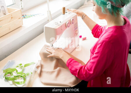 Hohen winkel Portrait von Kreative junge Frau, die Kleidung an der Nähmaschine sitzen und arbeiten in modernen Atelier, kopieren Raum Stockfoto