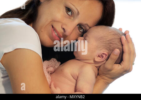 Schöne Mutter hält Ihr neugeborenes Baby in die Arme und blickt in die Kamera. Stockfoto