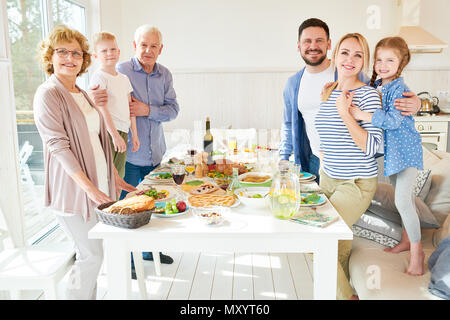 Portrait von glückliche zwei Generation Familie Abendessen zusammen posieren Runde festlichen Tisch mit leckeren Gerichten und lächelnd in die Kamera in der modernen Sun Stockfoto