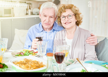 Portrait von Happy senior Paar posiert am Tisch lächelnd und Kamera während der Familienfeier zu Hause Stockfoto