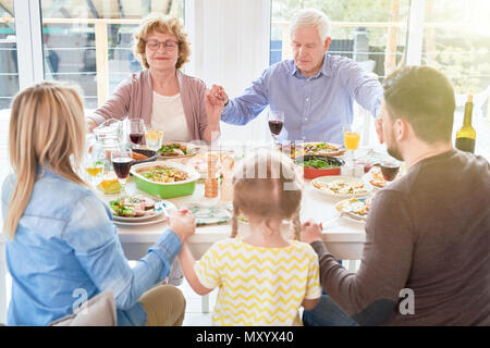 Portrait von großen glücklichen Familie verbinden Hände im Gebet zum Abendessen, das Hände während der festlichen Feier im Sonnenlicht Stockfoto