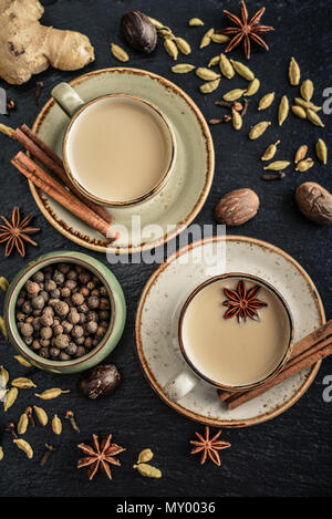 Traditionelle indische Getränk - Masala Chai Tee (Milch, Tee) mit Gewürzen auf schwarzem Schiefer Hintergrund, Ansicht von oben Stockfoto