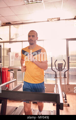 Ein junger Mann, tragen sportliche Kleidung, Traning auf Laufband, alte zusammengeschlagen Fitnessraum im Haus. Stockfoto